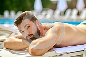 A dark-haired man sunbathing and looking relaxed