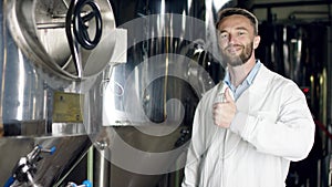 A dark-haired man in a white overall is being happy to work his shift at the brewery house and showing thumbs up, A