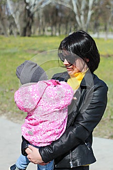 A dark-haired mother with glasses holds in her arms a child who hides her face