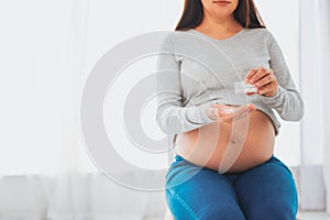 Dark-haired pregnant woman holding pills in her hands