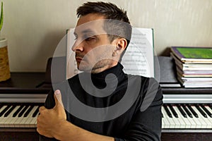 A dark-haired tanned young guy wearing a black turtleneck sitting with his back to the digital piano