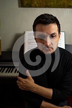 A dark-haired tanned young guy wearing a black turtleneck sitting with his back to the digital piano