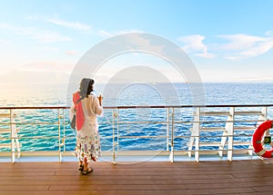 A dark haired woman on enjoys a drink on the deck of a cruise ship passing through the Greek Islands at sunset