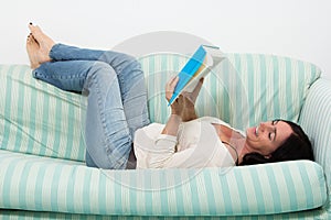 Dark haired woman lying on couch and reading a book