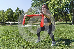 Dark haired woman practicing sport doing squats with a sport ribbon on her hands