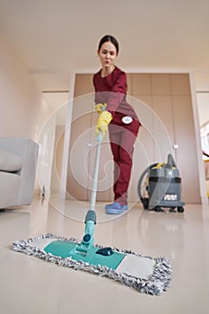 Dark-haired woman in rubber gloves mopping living room