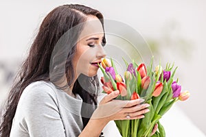 Dark haired woman smelling lovely aroma of fresh colorful tulips