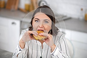 Dark-haired woman in a striped blouse eating a big burger