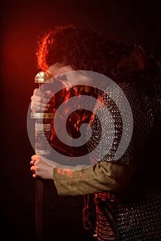 A dark-haired woman with a sword, a Scandinavian warrior in a chain mail against a dark background with red lights