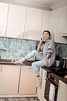 Dark-haired woman wearing jeans and warm socks sitting in the kitchen