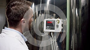 A dark-haired working man in a whie overall is checking the stability of readings a factory gear. A slow motion close up