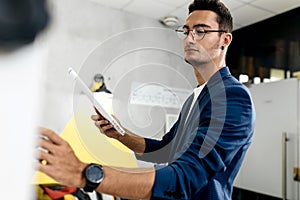 Dark-haired young architect dressed in blue checkered jacket works in the modern office