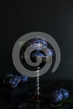 Dark juicy plums in silver bowl on a black background. Dark key
