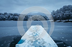 Dark landscape photo of mole pier covered of snow with frozen lake on background - winter time. Frozen and cold lake with hills