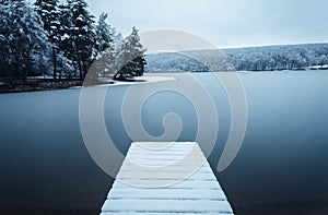 Dark landscape photo of mole pier covered of snow with frozen lake on background - winter time. Frozen and cold lake with hills