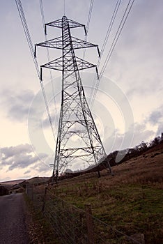 A dark large transmission tower, electricity pylon, stands against a yellow sunset.