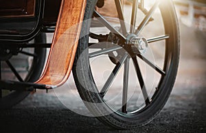 A dark large wheel on an ancient carriage for horses, which is illuminated by rays of sunlight. History