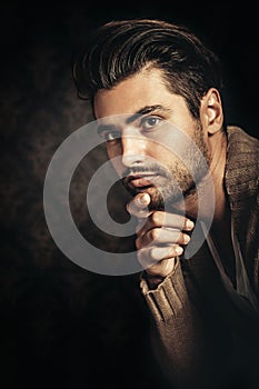 Dark light portrait of a young handsome man, hand under his chin.