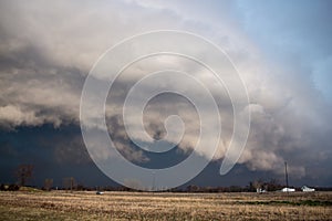 A dark, and menacing storm cloud races across flat farmland bringing dangerous wind and heavy rain.
