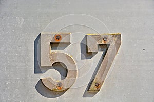 A dark metallic digit fixed on a wall and showing the number fifty seven