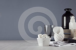 Dark minimalistic bathroom decor - dark glass vase, wood box, towel, products and accessories for care face skin on white wood.