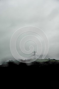 A dark moody blurred, edit of a electricity pylon silhouetted against storm clouds in the countryside. With raindrops on the