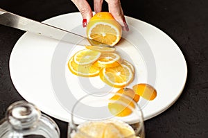 Dark moody. Food black background. On a white stone board in the hands of a girl, a knife cuts a lemon. Slices of lemon are piled