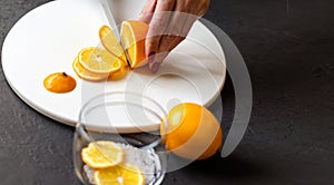 Dark moody. Food black background. On a white stone board in the hands of a girl, a knife cuts a lemon. Slices of lemon are piled