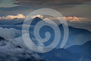 Dark mountains, autumn mist and sunlit clouds in Slovenian Alps