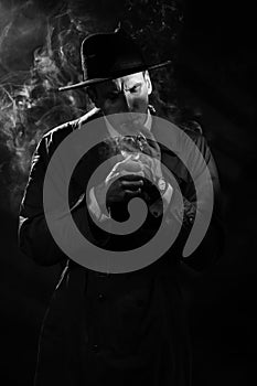 Dark noir portrait of a male detective lighting a cigarette. Private detective, spy, investigation concept.