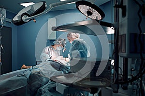 Dark operating room, surgeons make a complex ancological operation. Female team of surgeons. The concept of medecine.