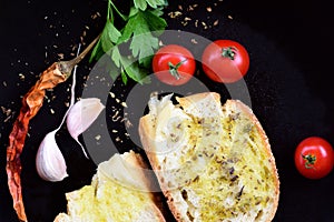 In a dark pan are two slices of white bread and olive oil, surrounded by peppers, tomatoes, garlic and parsley with oregano