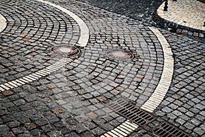 Dark paving stones with a pattern. Stone bridge road with sewer hatches. Street pavers