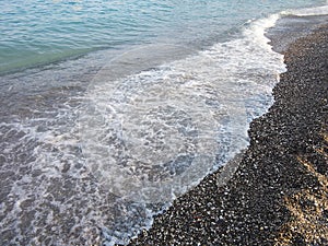 Dark pebbles beach and blue sea wave