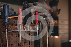 Dark photo of screw drivers hanging on the tool panel in old shed on sunset. Close up photo of colorful working tools on the wall