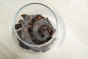 The dark pieces of dry food in glass jar on the light wooden table