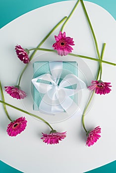 Dark pink gerberas on a table with beautiful present. Birthday Pastel Candy Blue Coloured Background.