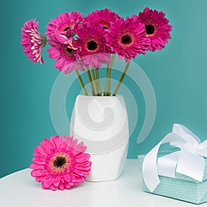 Dark pink gerberas in a vase on a table with beautiful present. Happy Mother`s Day, Women`s Day, Valentine`s Day or Birthday.