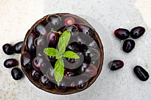 Dark pink-red ripe Syzygium cumini fruits. Dark black java plum in a wood bowl at isolated white background. Green mint leaf on
