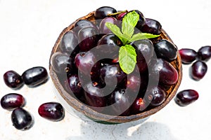 Dark pink-red ripe Syzygium cumini fruits. Dark black java plum in a wood bowl at isolated white background. Green mint leaf on