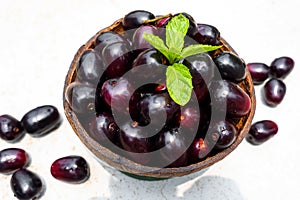 Dark pink-red ripe Syzygium cumini fruits. Dark black java plum in a wood bowl at isolated white background. Green mint leaf on