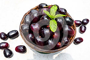 Dark pink-red ripe Syzygium cumini fruits. Dark black java plum in a wood bowl at isolated white background. Green mint leaf on