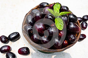 Dark pink-red ripe Syzygium cumini fruits. Dark black java plum in a wood bowl at isolated white background. Green mint leaf on