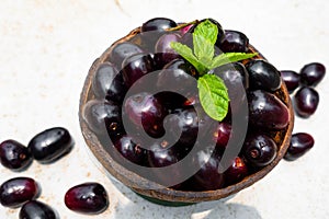 Dark pink-red ripe Syzygium cumini fruits. Dark black java plum in a wood bowl at isolated white background. Green mint leaf on