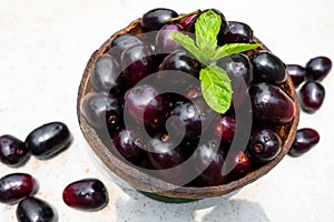 Dark pink-red ripe Syzygium cumini fruits. Dark black java plum in a wood bowl at isolated white background. Green mint leaf on