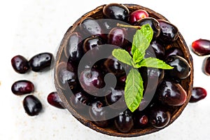 Dark pink-red ripe Syzygium cumini fruits. Dark black java plum in a wood bowl at isolated white background. Green mint leaf on