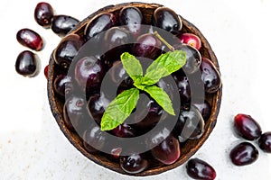 Dark pink-red ripe Syzygium cumini fruits. Dark black java plum in a wood bowl at isolated white background. Green mint leaf on