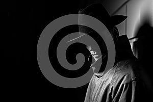 Dark portrait of a man in a raincoat with a hat at night on the street