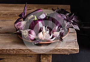 Dark purple peppers with leaves of basil and garlic on old rustic wooden table