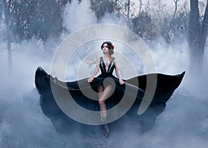 The dark queen, with bare long legs, walks fog. A luxurious black dress flares in different directions, like the wings